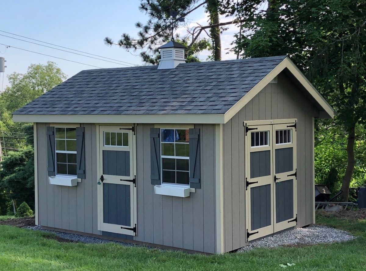 Amish garden shed kit with double doors, window shutters, and a shingle roof.