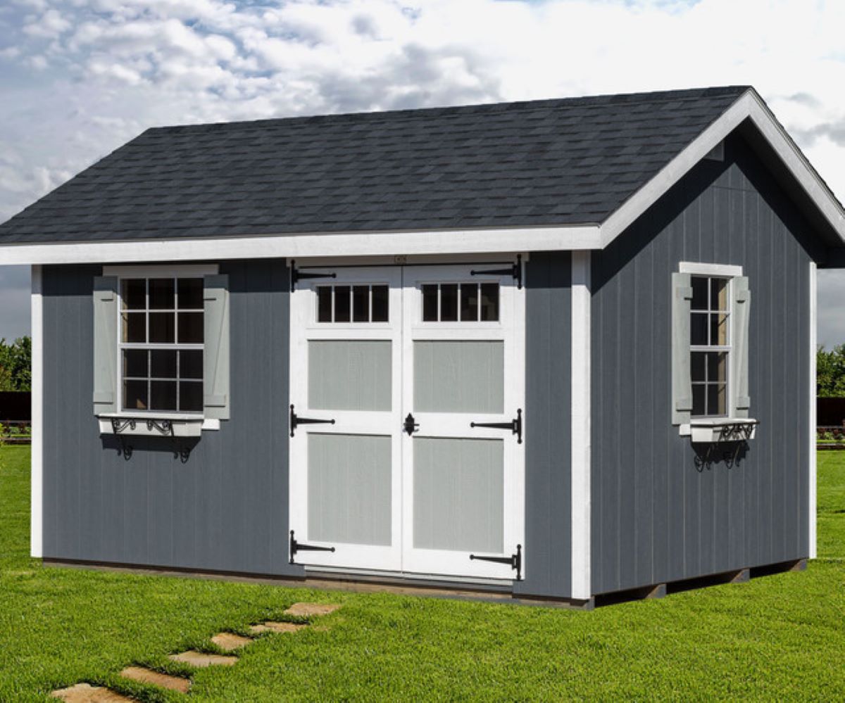 Gray Amish shed with white trim, double doors, shutters, and shingle roof on lawn.