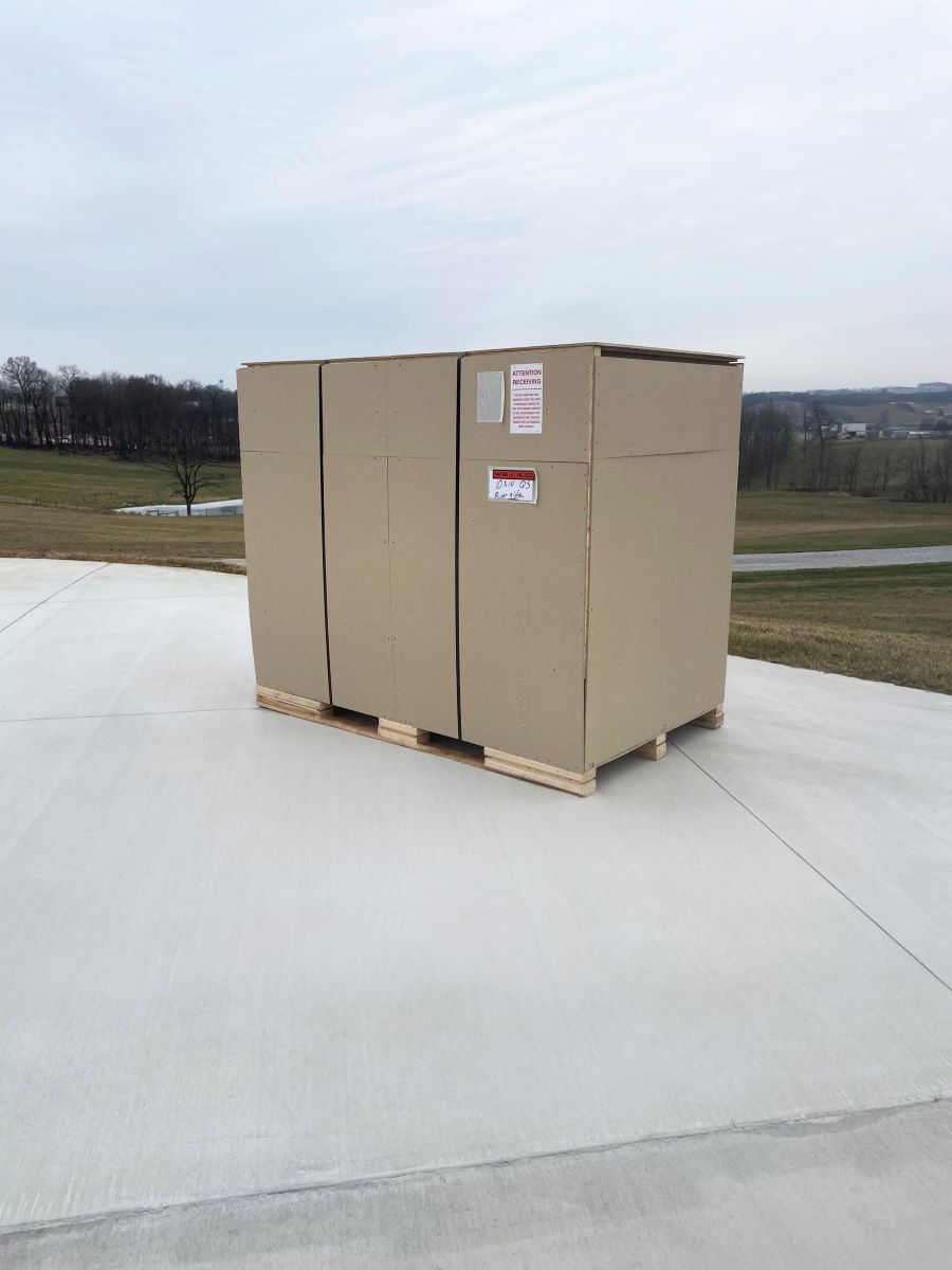 Palletized shed kit crate on a concrete driveway, labeled for curbside home delivery.